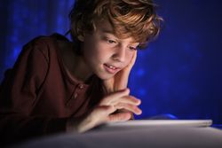 Cheerful boy using tablet on bed at night