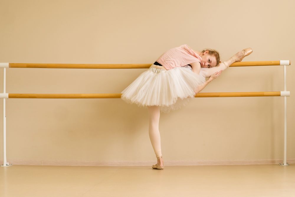 Ballet dancer rests on barre, holding stretch with leg raised