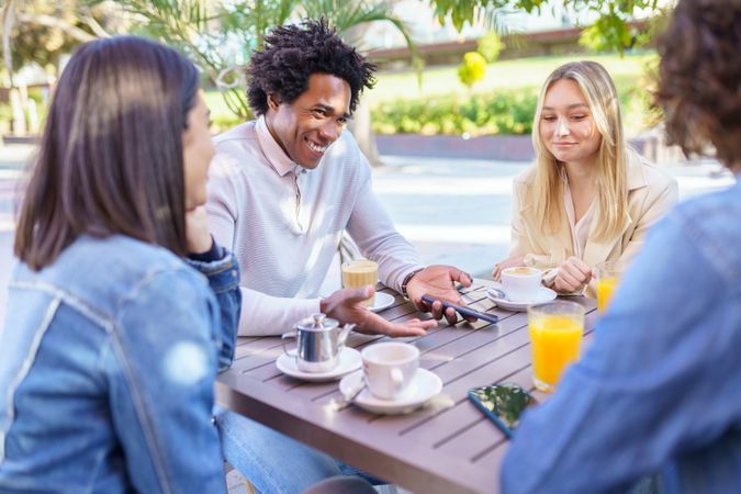 Multi-ethnic friends laughing over coffee and juice at outside table
