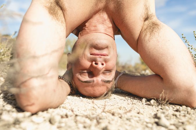 Close-up of a gray-haired man in Salamba Shirshasana pose during a yoga session in nature