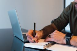 Anonymous man writing in notebook near laptop