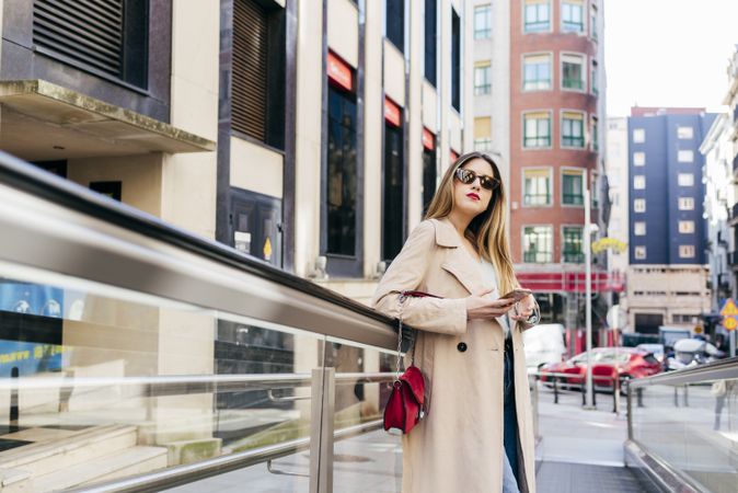 Young cheerful female leaning on stairs with smartphone