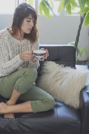 Curious female on cozy sofa with cup of tea, copy space