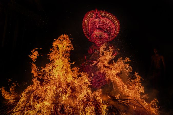 Man performing Theyyam ritual form of dance worship surrounded by fire at night