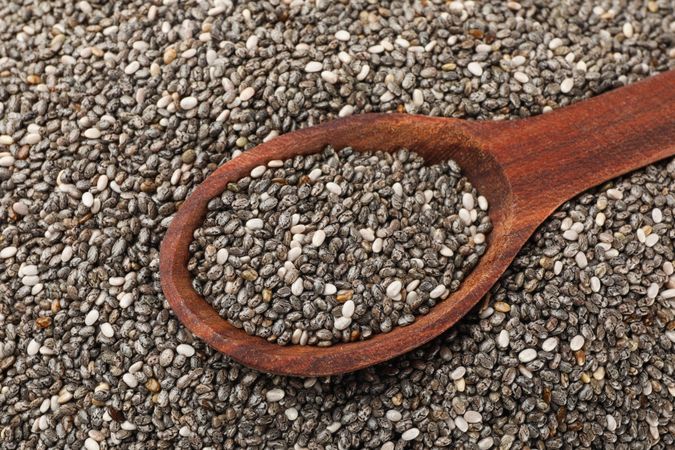 Chia seeds and wooden spoon textured background, close up
