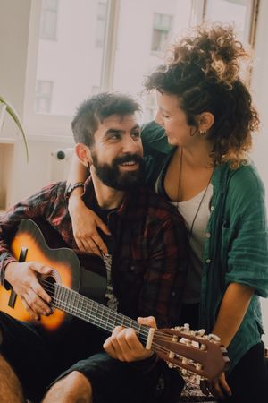 Cheerful couple playing guitar at home