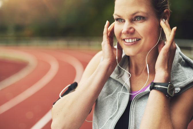 Woman smiling while listening to earphones in ear on race track