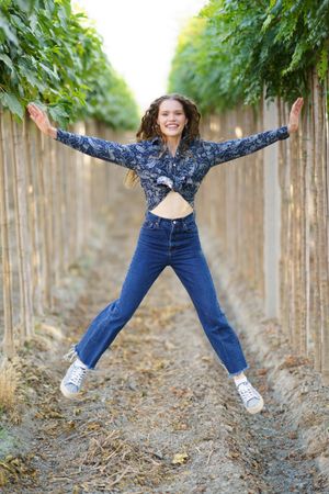 A Joyful Young Woman is Joyfully Jumping in a Vineyard Surrounded by Lush Green Rows