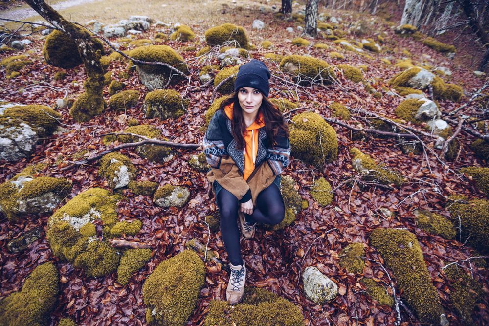 Bored female tourist resting on rock at autumn forest