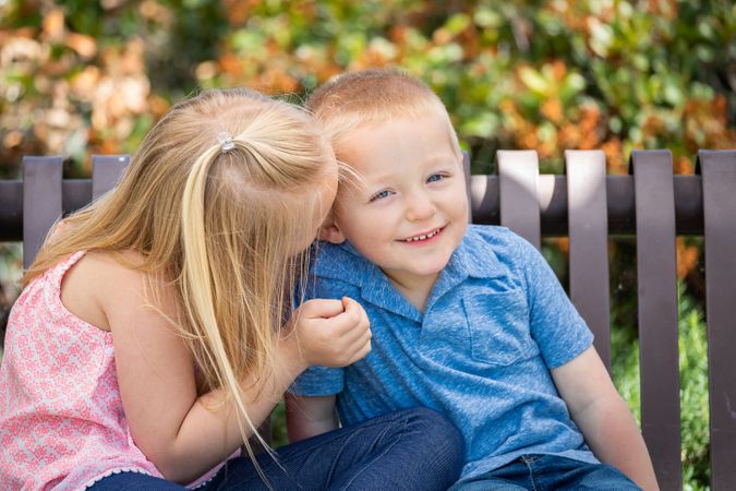 Young Sister and Brother Whispering Secrets On The Bench At The Park