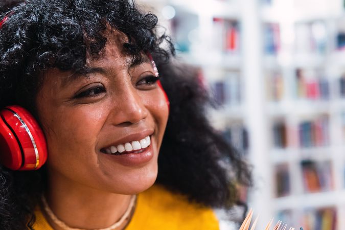 Delighted female student listening to song in headphones in library