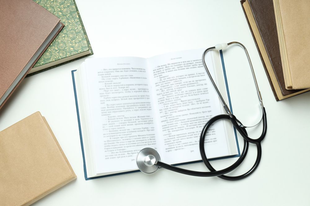 Books and stethoscope on light background, top view
