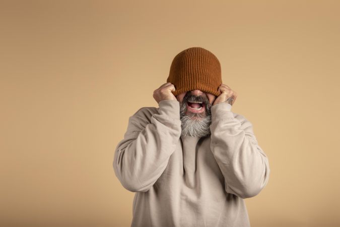 Studio portrait of an over excited man hiding his eyes with brown knit cap