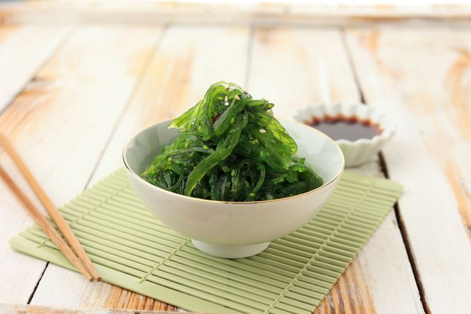 Bowl of Japanese seaweed salad on mint placemat with chopsticks