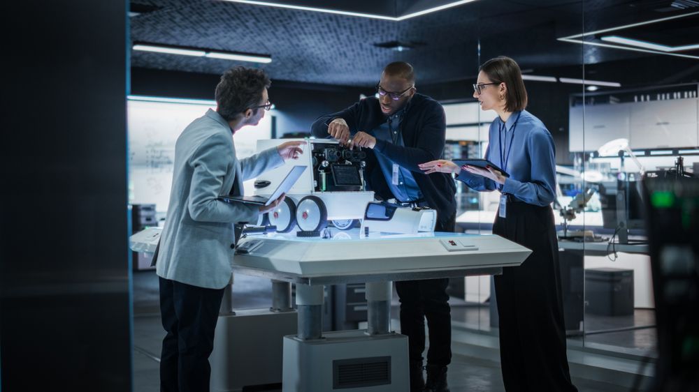 Software Engineer Working on a Computer Behind the Desk. Diverse Team of Industrial Specialists Working on Remotely Controlled Mobility Robot in a Research Facility