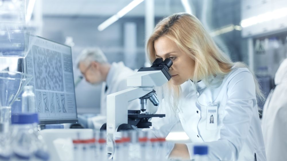 Female Research Scientist Looks at Biological Samples Under Microscope.