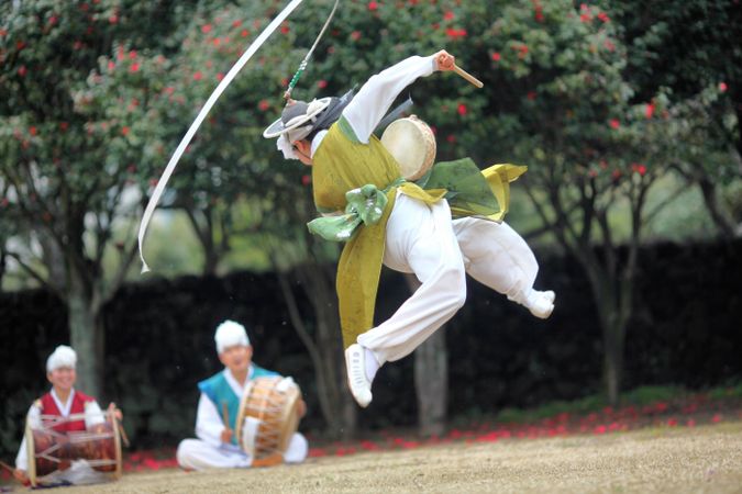 Korean man in hanbok performing while other men playing drums outdoor