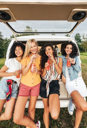 Group of diverse women holding cocktails while standing at the back of camper van