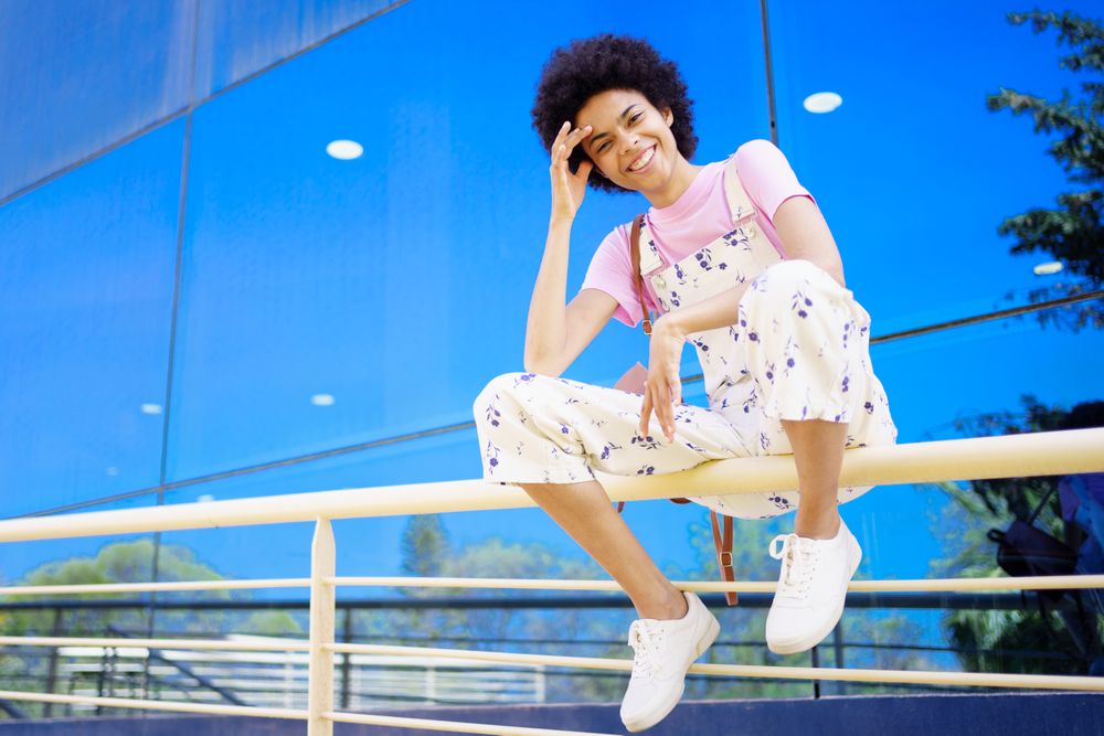 Smiling woman sitting on handrails in front of reflective building