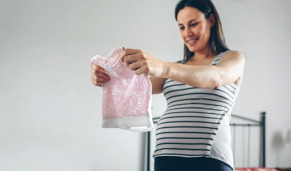 Pregnant person looking at baby girl dress