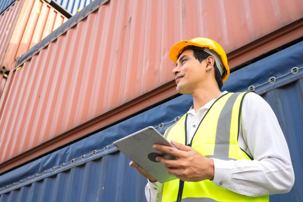 Asian engineer with digital tablet standing near containers