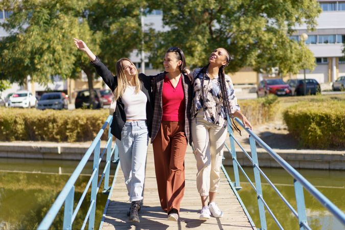 Three women happily walking over pedestrian bridge on summer’s day