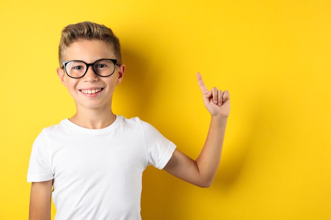 Happy boy in glasses against yellow background, space for text