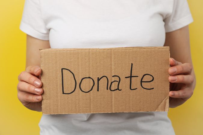 Woman holds cardboard with text Donate on yellow background