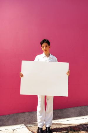 Serious male holding blank placard against a pink background
