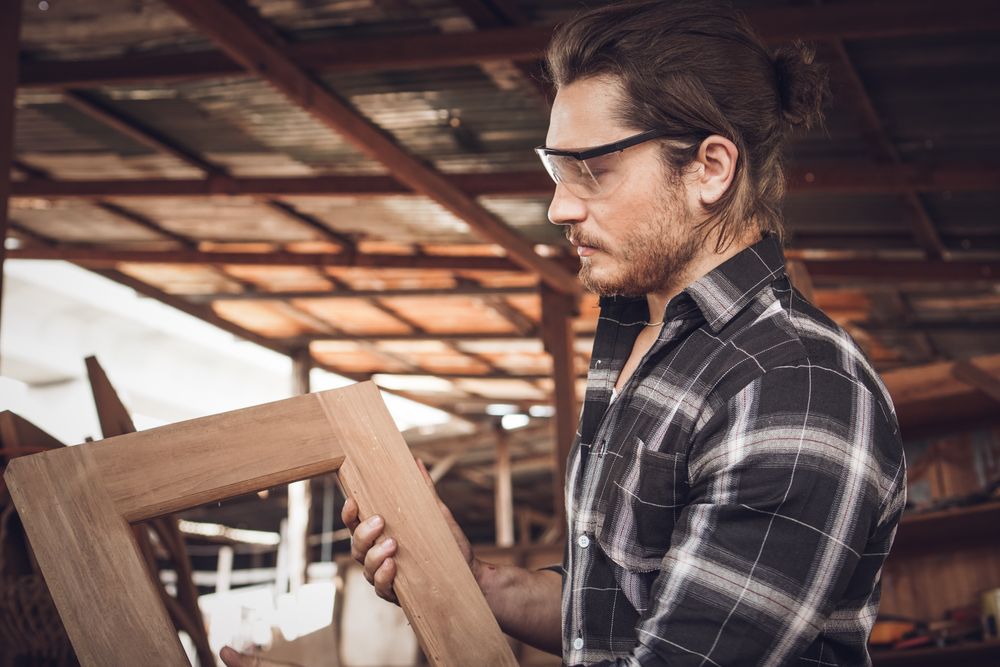 Male woodworker holding up a wooden frame he made in his workshop