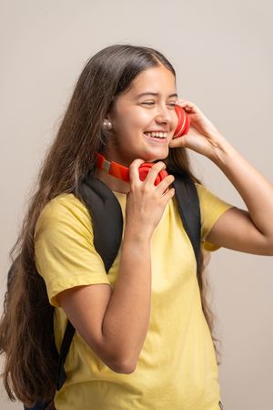 A happy young student laughs while putting on red headphones to listen to music.
