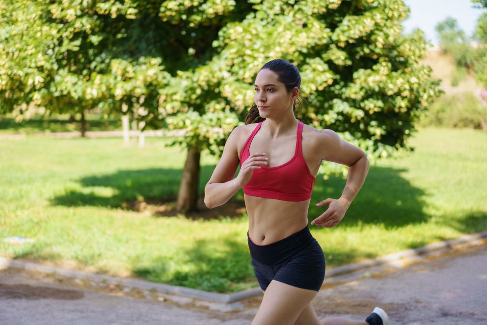 A young woman is running outdoors in a park, dedicated to fitness and maintaining a healthy lifestyle