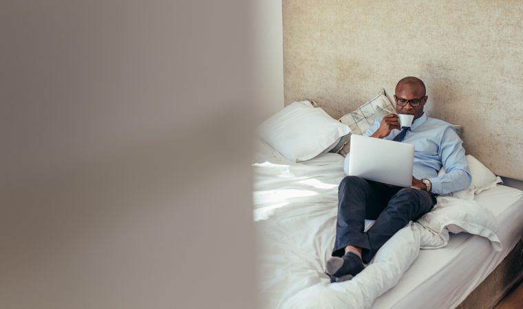 Man in formal clothes working on laptop while lying in bed