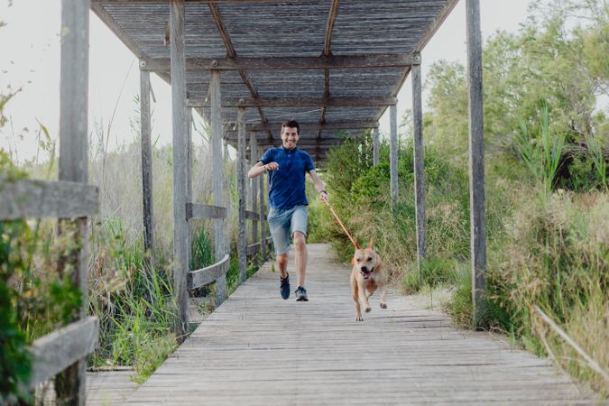 Happy adult man running with dog along countryside