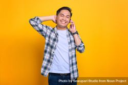 Smiling Asian male talking on phone in studio shoot with hand behind his head 4NLXg0
