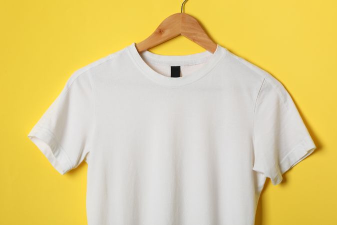 Hanger with blank plain t-shirt on yellow background, space for text