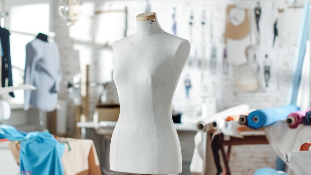 Shot of a Tailoring Mannequin that Stands in a Bright and Sunny Studio. Various Sewing Items and Colorful Fabrics Laying around