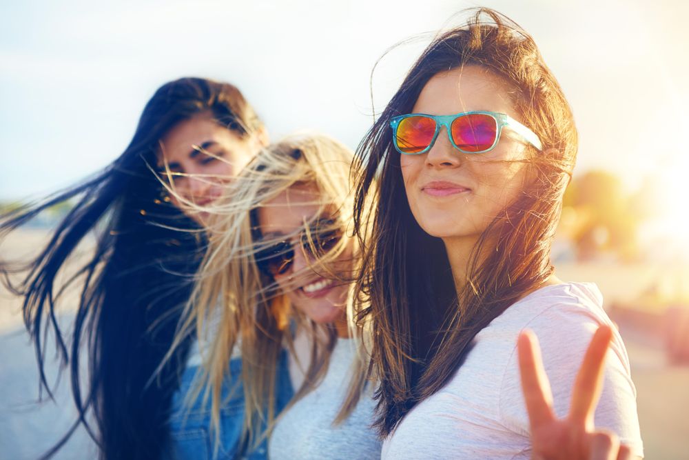 Happy multi-ethnic female friends sitting in sunny field with one making the peace sign with hand