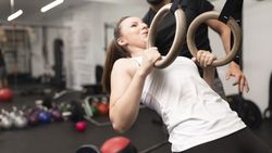 Young woman performs arms exercise on gymnastic rings at fitness center