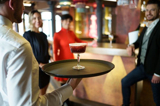 Bartender with red cocktail on serving tray