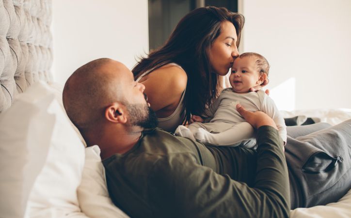 Parents with their newborn baby boy on bed at home