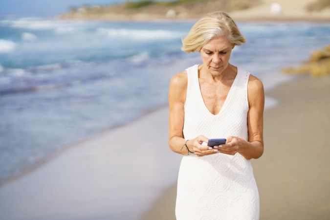 Mature woman using her phone on a rocky beach