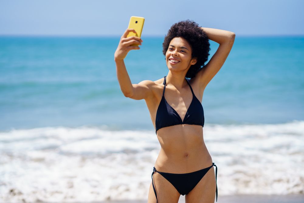 Happy woman in biking standing near the ocean taking a selfie on vacation