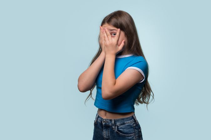 Girl covering face with hands, peeking through fingers.