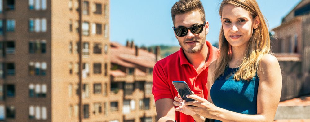 Young couple with mobile looking at camera in rooftop on a summer day
