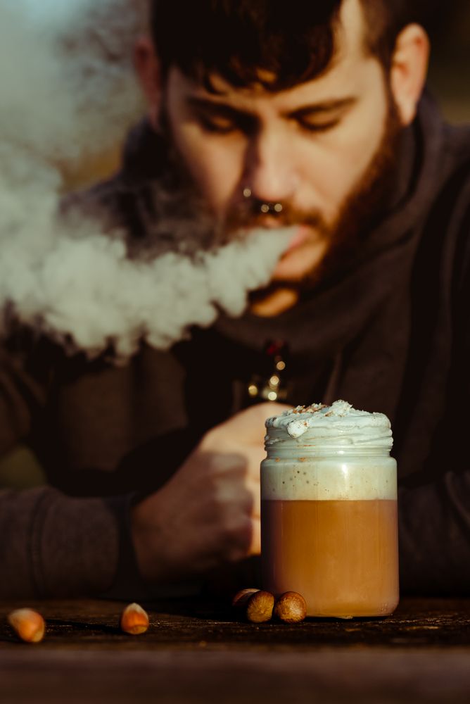 Vaper puffing smoke near a cup of fresh coffee