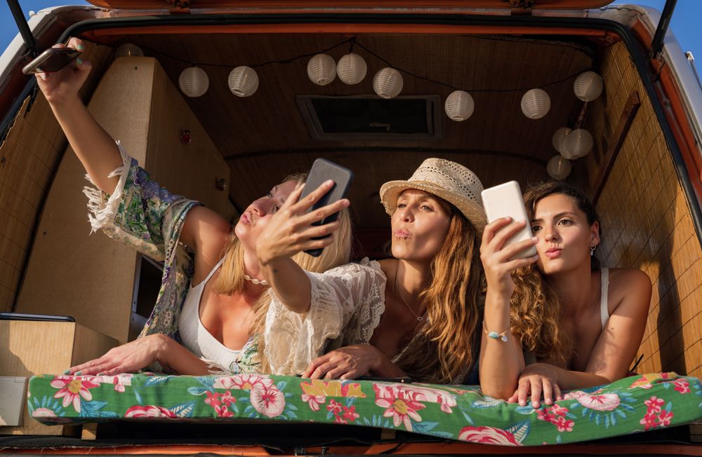 Relaxed female friends taking selfie comfortable placing on trunk of blue car