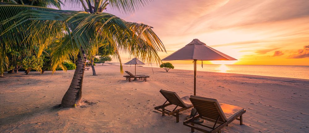 Tropical beach at sunset with two chairs and an umbrella