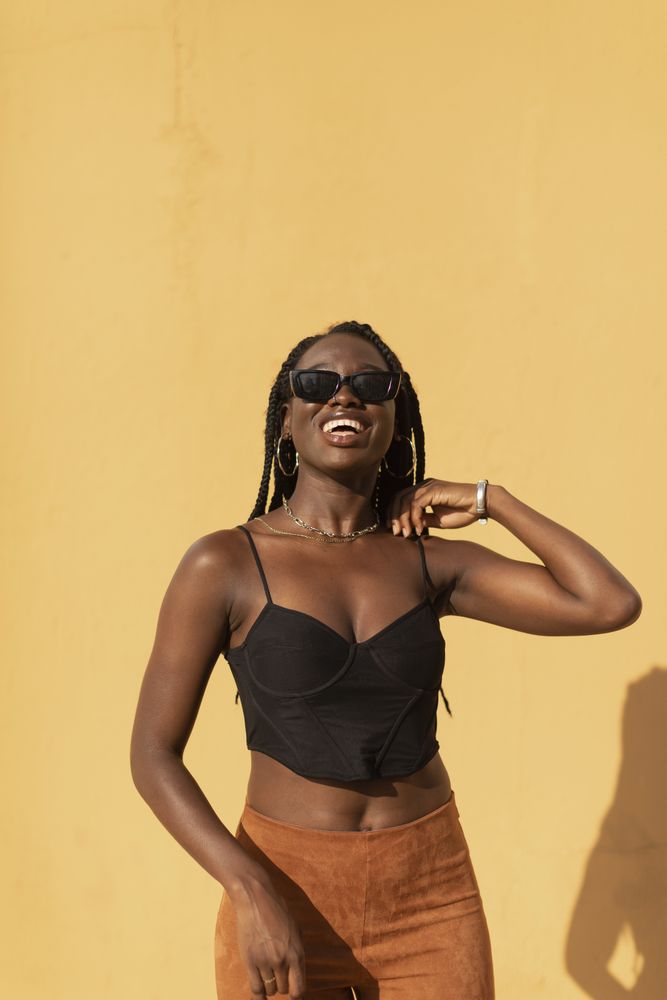 Portrait of a young Black female posing with style and smiling with a plain orange wall behind her