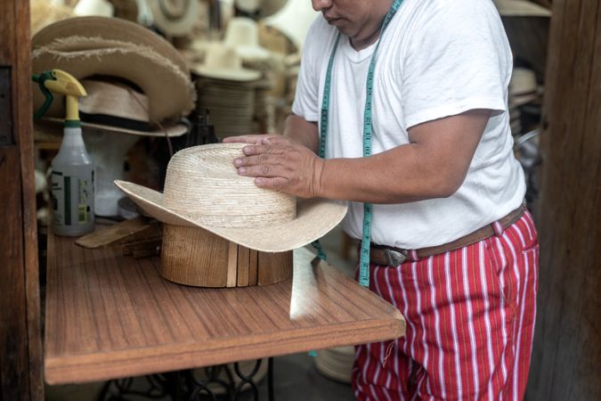 An adult Hispanic man is shaping a natural fiber hat